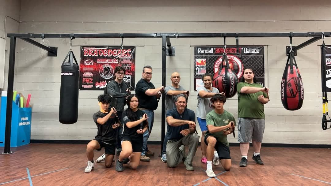 Group of Serrada Escrima students holding training sticks in a crossed salute in a martial arts gym
