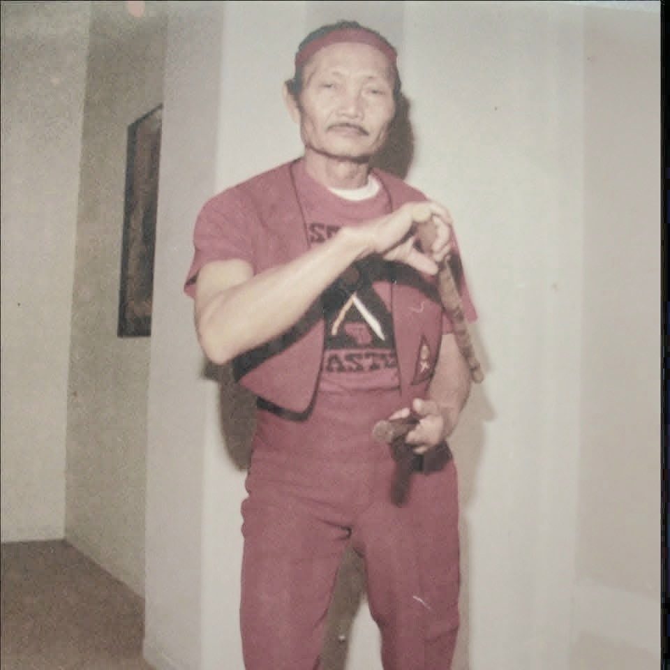 Vintage color photo of Great Grandmaster Angel Cabales in a red uniform holding an Escrima stick and dagger