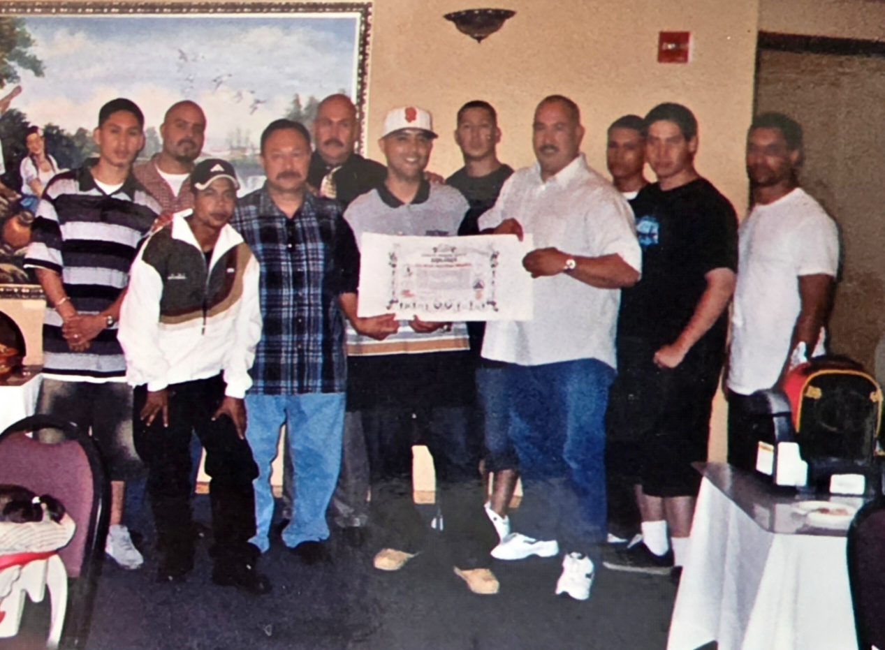 Group of Serrada Escrima practitioners gathered around a Masters Degree certificate at a celebration dinner